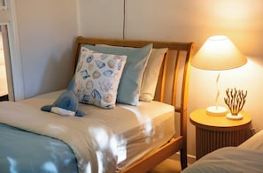 Una cama con un cojín de estampado azul y blanco, un cabecero de madera y una lámpara de noche con un detalle coral.