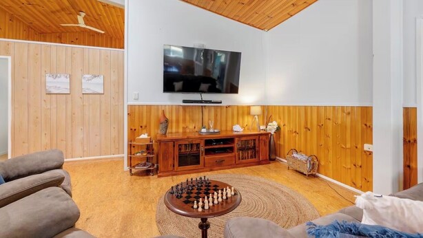 A living room with a wooden ceiling, a flat-screen TV mounted on the wall, a wooden entertainment unit, and a round coffee table with chess pieces. - The big catch! - 3.5 acres - pets! - boats - fishing and crabbing! (Rodds Bay)
