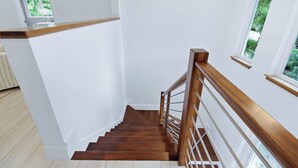 Una escalera de madera con barandilla blanca y vista a la vegetación exterior.