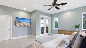 Un dormitorio con cama, ventilador de techo, televisor y vistas al exterior.