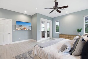 Ein Schlafzimmer mit Bett, Deckenventilator, Fernseher und Blick ins Freie.