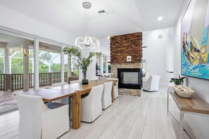 Een modern interieur met een eethoek, een open haard en een groot raam met uitzicht op groen.