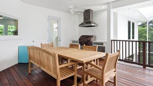 Un espacio comedor al aire libre con techo, una mesa y sillas de madera, una parrilla y un ventilador de techo.