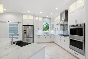 A modern kitchen with white cabinetry, stainless steel appliances, and a large window. - Pine Sanibel - Where Beachfront Living Meets a Boater’s Paradise (Sanibel)