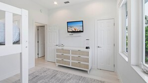 Un interior moderno con un televisor montado en la pared, una consola blanca y una puerta que da a otra habitación.