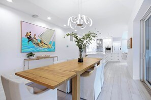 A modern kitchen with white cabinetry, a wooden dining table, and a large painting of a sailing boat. - Pine Sanibel - Where Beachfront Living Meets a Boater’s Paradise (Sanibel)