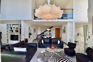 A modern living space with a black leather sofa, a zebra-patterned rug, and a dining area with a staircase. - PRESTIGE RANGE - VACATION RENTALS IN ROYAN AND PONTAILLAC - 2-BEDROOM APARTMENT (Royan)