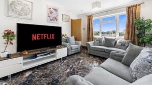 Sala de estar con un televisor de pantalla plana grande, dos sofás grises, una mesa de centro y piso de mármol.