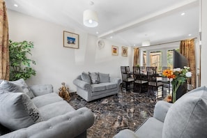 A living room with a grey sofa, a dining table with chairs, a potted plant, and a fireplace. - Modern Home | Private Parking & Garden | Office (New Addington)