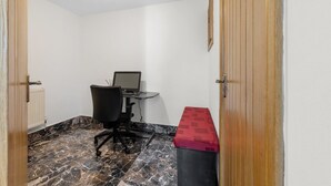 Una habitación con escritorio, silla y computadora. Se observa un radiador y una puerta con marco de madera.