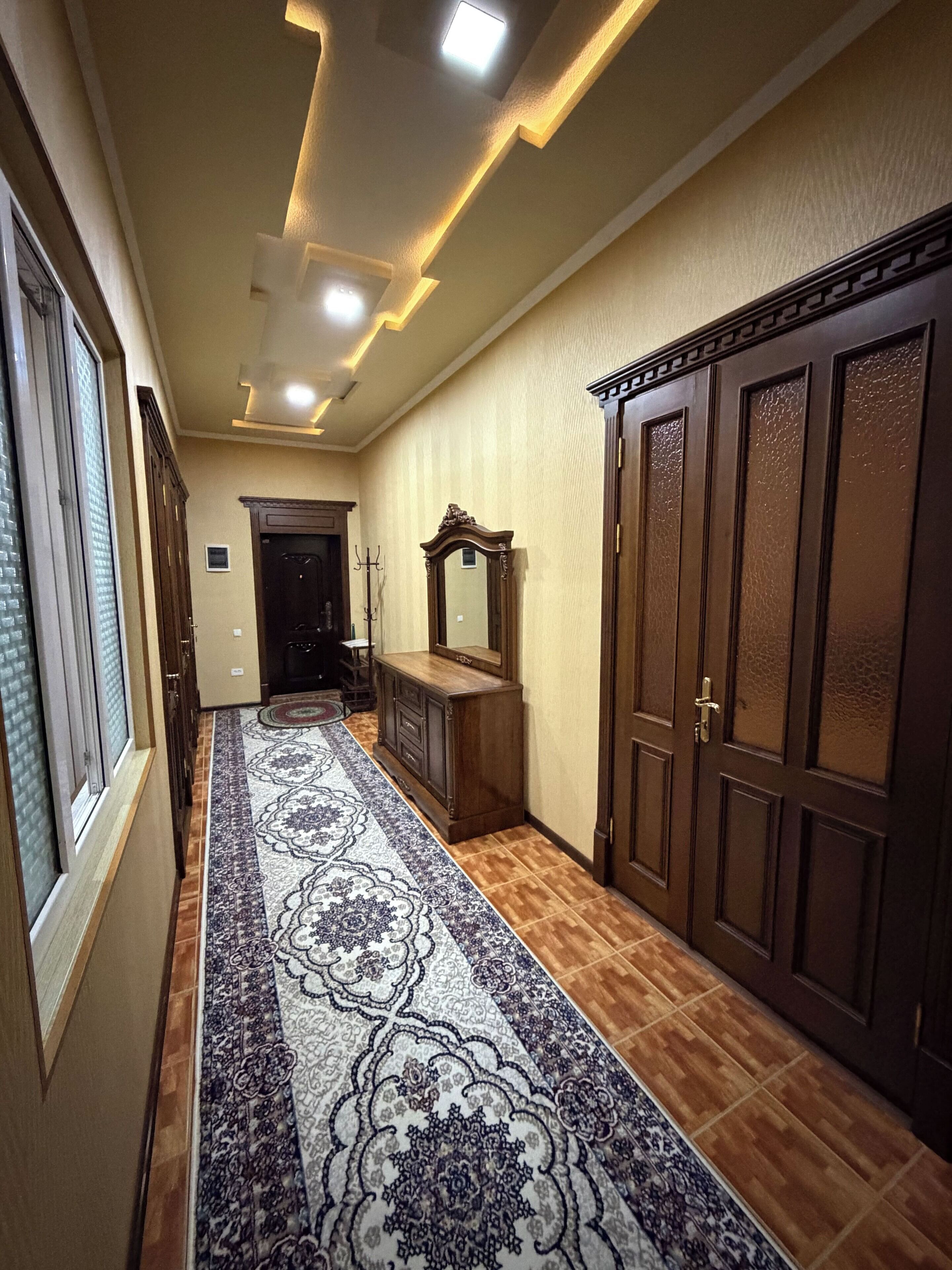 A hallway with a patterned carpet, wooden wardrobe, and a mirror.