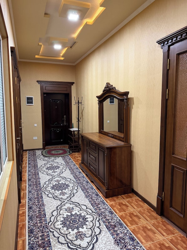 A hallway with a patterned carpet, a wooden cabinet, a mirror, and a door.