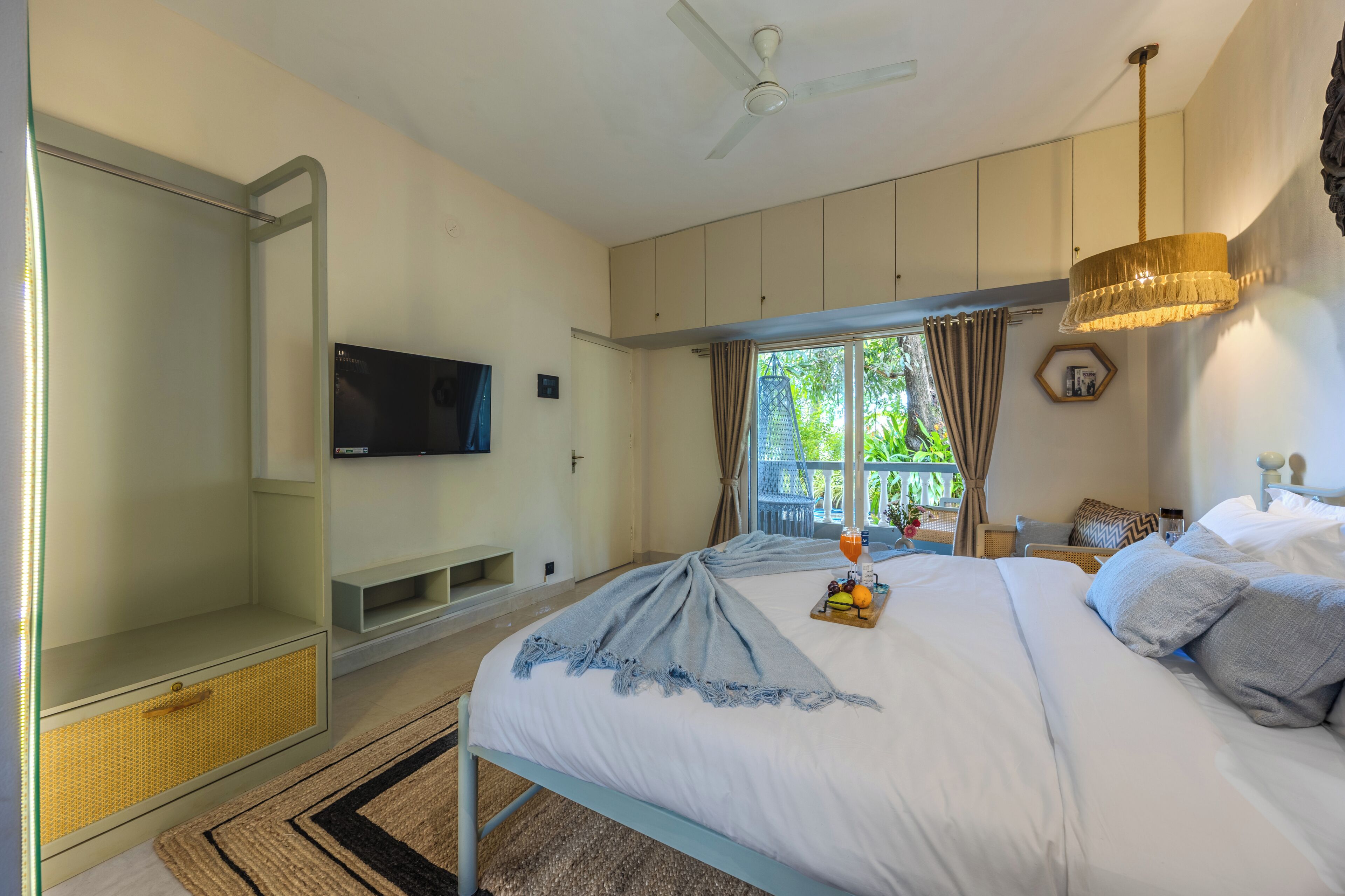 A bedroom with a bed, a TV, a ceiling fan, and a window with curtains.
