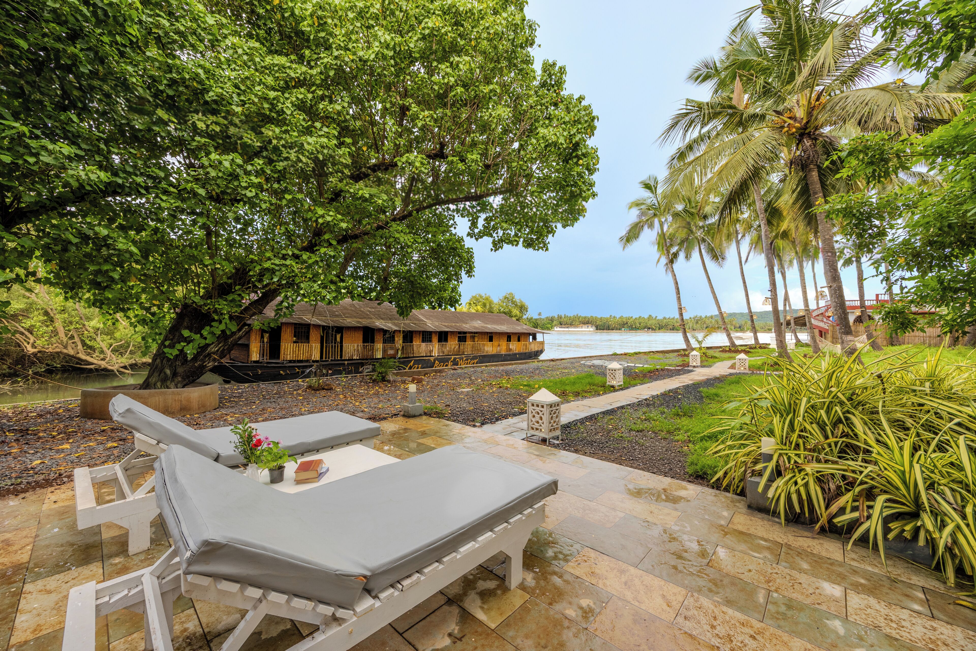 A serene outdoor seating area with a view of a river and a thatched-roof structure.