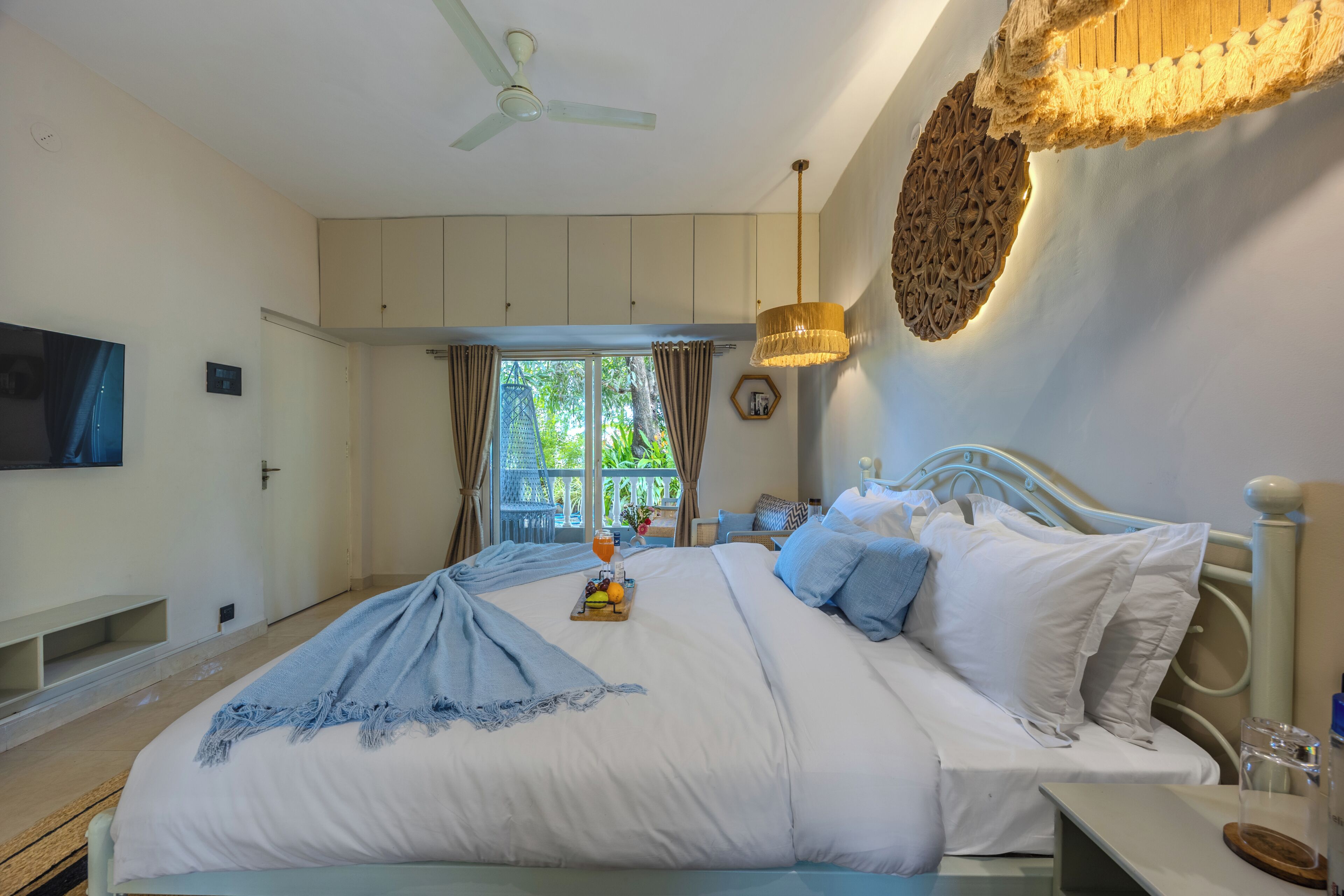 A bedroom with a bed, a television, a ceiling fan, and a window with curtains.