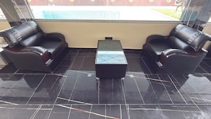 Uma área de estar com duas poltronas de couro preto e uma mesa com tampo de vidro, com vista para um edifício e uma cerca.