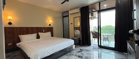 Habitación de hotel con cama, ventilador de techo, suelo de mármol y balcón con mesa y sillas.