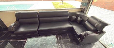 Un sofá de cuero negro con una mesita de centro de vidrio en una habitación con piso de baldosas.