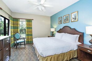 A hotel room with a bed, a chair, a desk, a nightstand, a lamp, and a ceiling fan. - Sunshine, Stretch Out, Repeat 1 BR Suite (Kissimmee)
