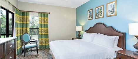 Habitación de hotel con cama, una silla, escritorio, mesita de noche, lámpara y ventilador de techo.