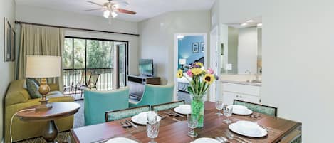 A dining area with a table set for four, a ceiling fan, and a view of a balcony with outdoor furniture.
