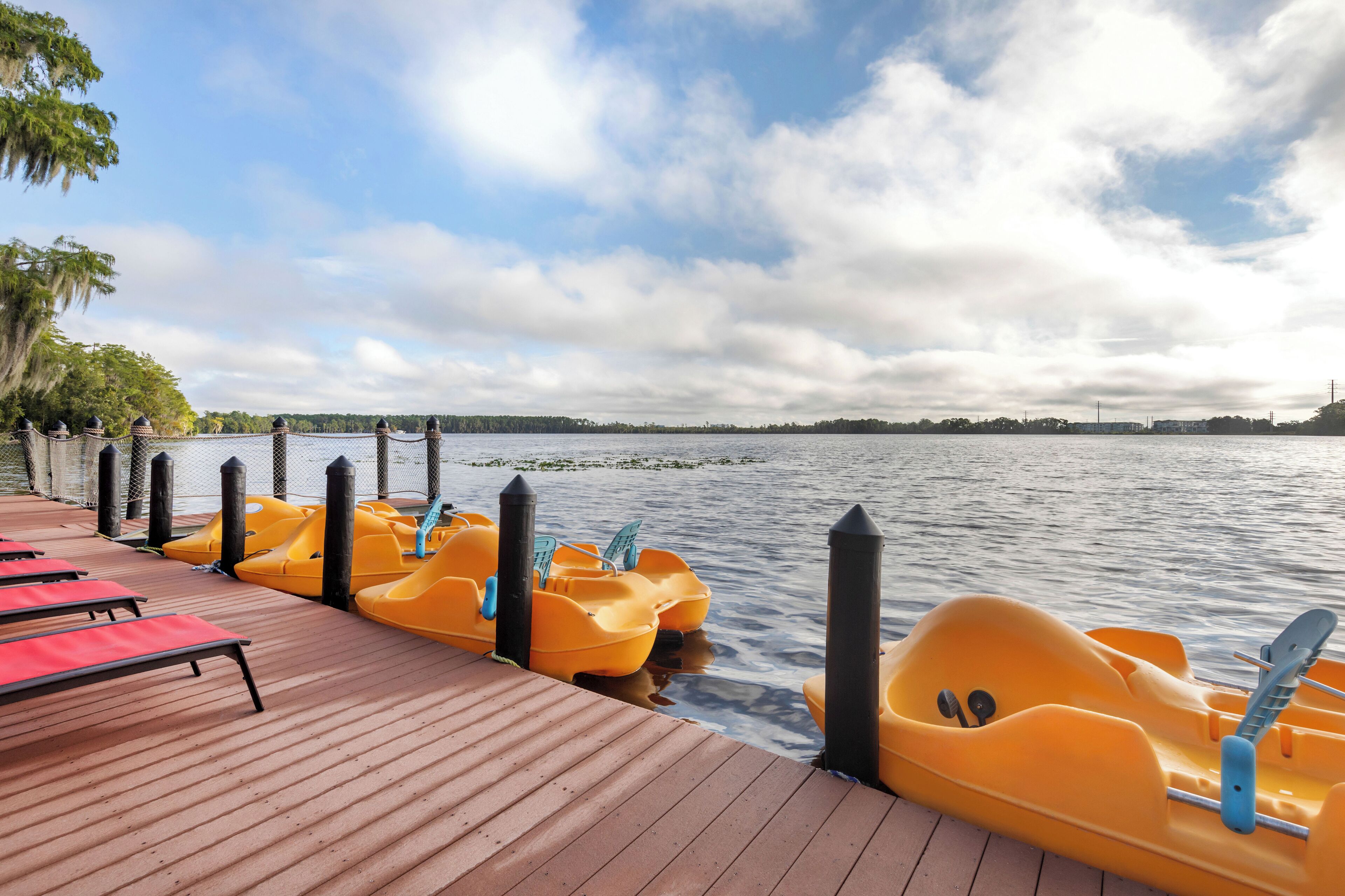 A wooden dock with yellow paddle boats and red lounge chairs.