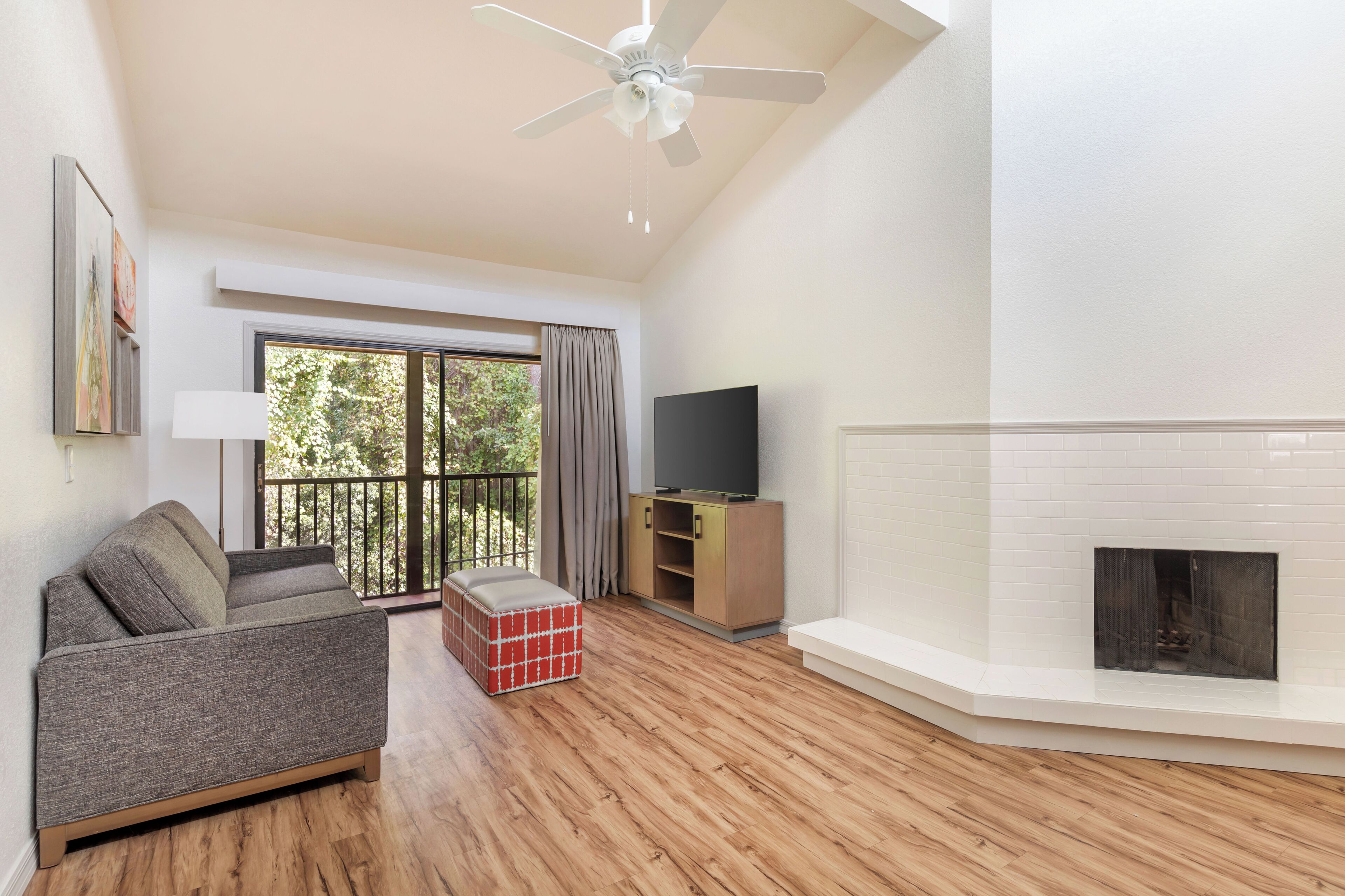 Ein Wohnzimmer mit einer Couch, einem Fernseher, einem Kamin und einem Balkon mit Vorhängen.