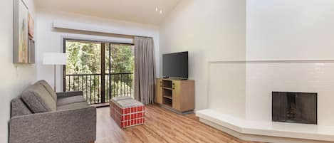 A living room with a sofa, a television, a fireplace, and a balcony with curtains.