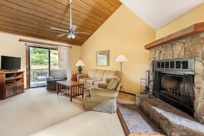 A cozy living room with a stone fireplace, a ceiling fan, a television, and a sofa.