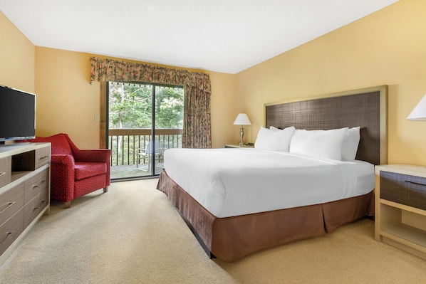 A hotel room with a large bed, a TV, a red chair, a balcony with a view, and a lamp.