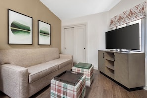 Un salon avec un canapé beige, une table basse, un téléviseur posé sur un meuble en bois et deux tableaux encadrés accrochés au mur.