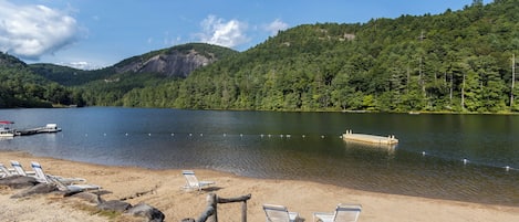 A lakeside beach with lounge chairs and a dock.