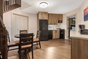 A modern kitchen with wooden cabinets, a black refrigerator, and a dining area with a round table and chairs. - Relax, Recharge & Explore Sapphire | 1BR Fireplace Retreat (Sapphire)