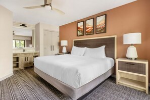 Une chambre d’hôtel avec un grand lit, deux tables de chevet avec des lampes, un ventilateur de plafond, une armoire et une fenêtre avec des rideaux.