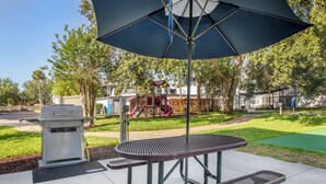Een terras met een tafel en banken, een overdekte picknicktafel en een barbecue.