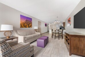 A modern living room with a sofa, a coffee table, and a dining area with chairs and a table. - Spacious 2BR Resort Near Disney | Pool + Private Balcony (Kissimmee)
