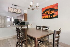 A modern kitchen with a dining area, including a table with chairs and a painting of an elephant. - Spacious 2BR Resort Near Disney | Pool + Private Balcony (Kissimmee)