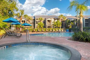 A swimming pool area with lounge chairs and umbrellas, surrounded by buildings with balconies. - Spacious 2BR Resort Near Disney | Pool + Private Balcony (Kissimmee)