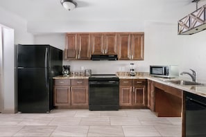 A modern kitchen with wooden cabinets, a black refrigerator, a microwave, and a stainless steel sink. - More Space, More Memories | Family 2BR Resort Near Disney (Kissimmee)