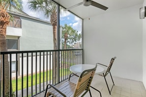 A balcony with a table and chairs, a ceiling fan, and a view of palm trees and buildings. - More Space, More Memories | Family 2BR Resort Near Disney (Kissimmee)