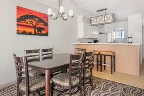 Ein Essbereich mit Holztisch und -stühlen, eine Küche mit weißen Schränken und ein zebra-gemustertes Teppich.