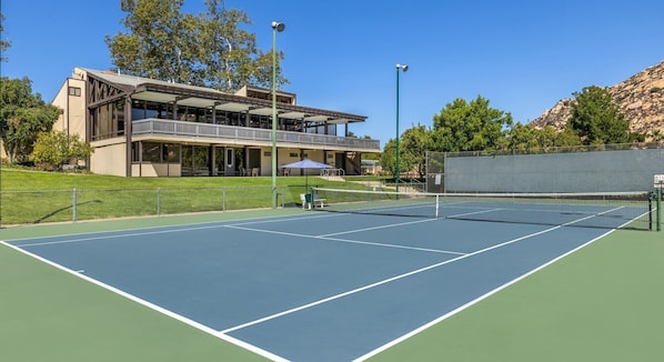 An outdoor tennis court with a building in the background.