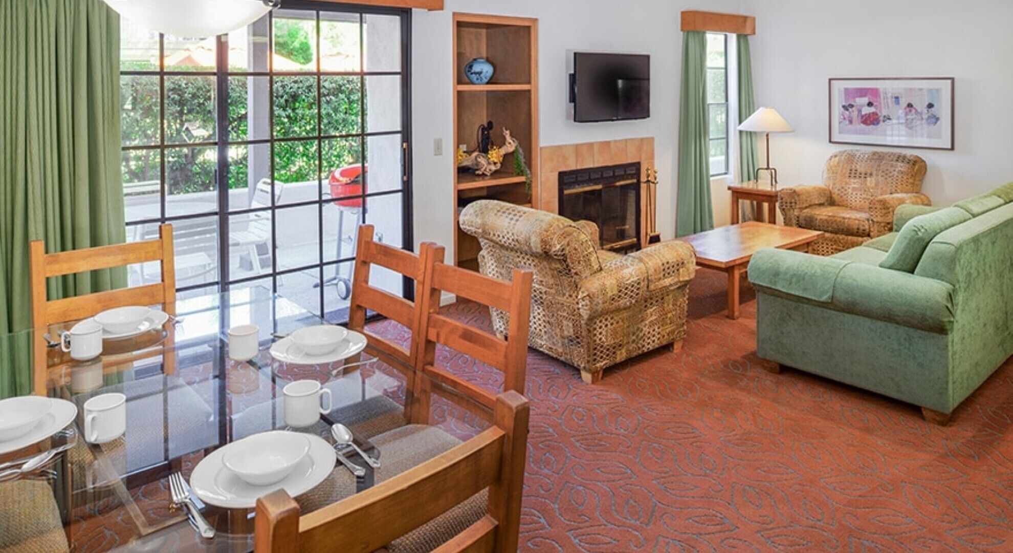 Um quarto com uma mesa de jantar posta para quatro pessoas, um sofá, uma lareira e uma televisão fixada na parede.