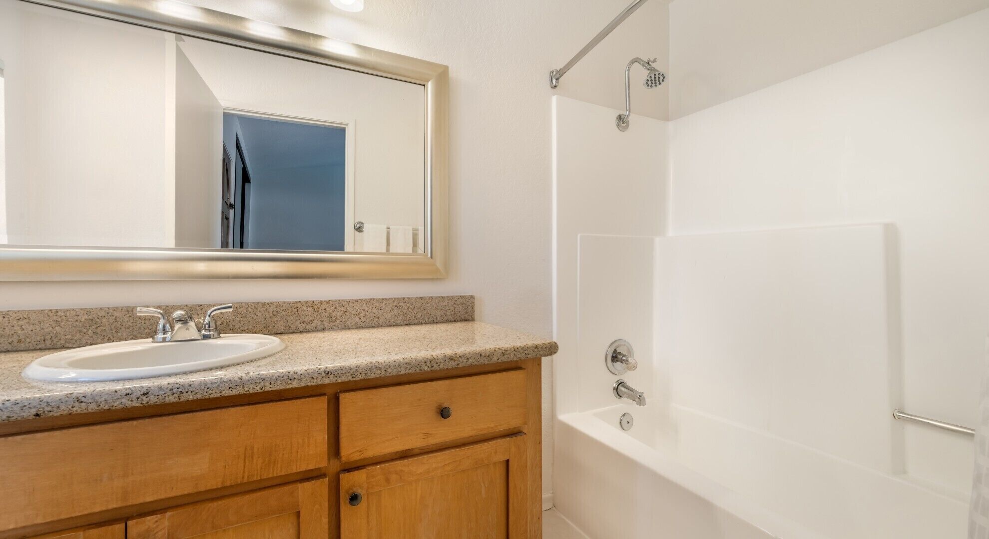 Een badkamer met een witte wastafel, een houten wastafelmeubel en een douche.