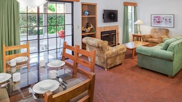 A room with a dining table set for four, a sofa, a fireplace, and a television mounted on the wall.
