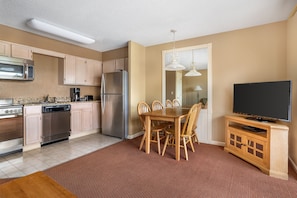 A compact kitchen with modern appliances, a dining area with a wooden table and chairs, and a flat-screen TV on a wooden cabinet. - Relaxing 1BR Retreat Minutes from Dollywood (Pigeon Forge)
