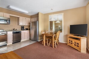 A compact kitchen with modern appliances, a dining area with a wooden table and chairs, and a flat-screen TV on a wooden cabinet. - Explore Pigeon Forge from This Cozy 1BR Retreat (Pigeon Forge)