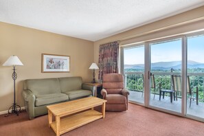 A living room with a sofa, armchair, and a table. There is a large window with a view of mountains. - Explore Pigeon Forge from This Cozy 1BR Retreat (Pigeon Forge)