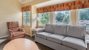 A living room with a brown leather armchair, a grey sofa, a round wooden table, and a lamp on a small table. - Convenient 2BR Cottage Near Dollywood & Dining (Pigeon Forge)