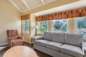 A living room with a brown leather armchair, a grey sofa, a round wooden table, and a lamp on a small table. - Private 2BR Smoky Mountain Cottage Near Dollywood (Pigeon Forge)